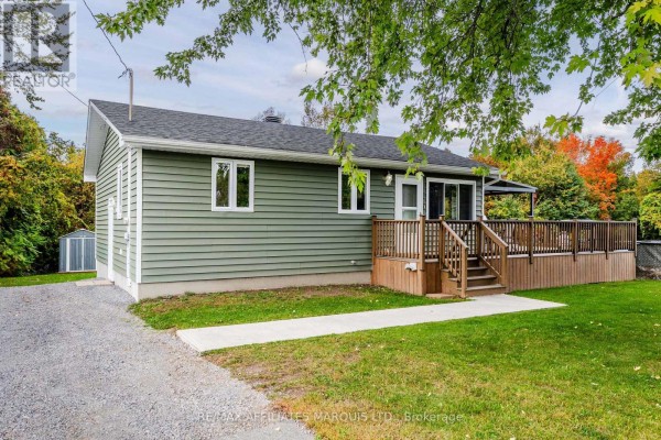 Side view of green house with wood deck and steps. Gravel driveway on left. - 20251 Kenyon Conc Rd 1 Concession, North Glengarry