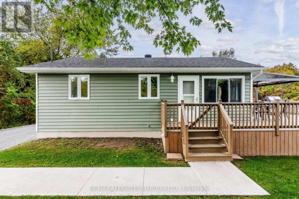 Front view of green house with wood deck and stairs. Sliding glass door visible. - 20251 Kenyon Conc Rd 1 Concession, North Glengarry