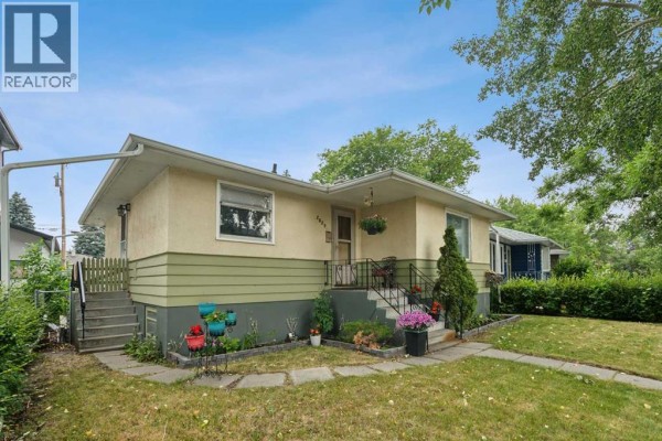Side exterior view of a bungalow with light beige and green siding, a pathway, and surrounding greenery. - 2029 Mountview Crescent Ne, Calgary