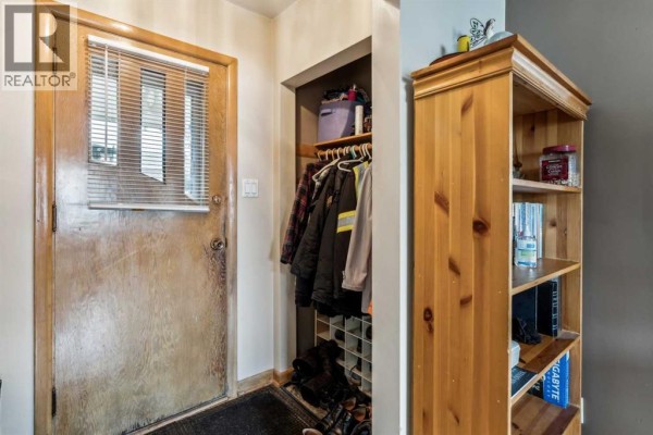 Interior entryway with a wooden door, a coat closet with hanging clothes, and a wooden bookshelf. - 2029 Mountview Crescent Ne, Calgary