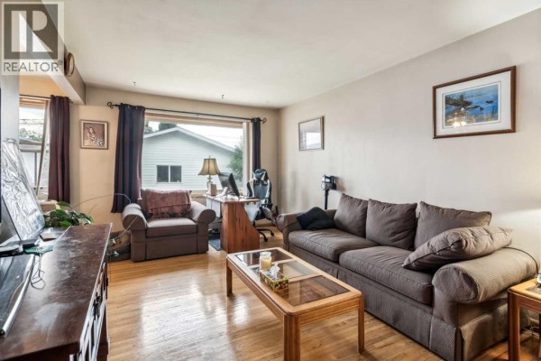 Living room with a sofa, armchair, desk, and a large window overlooking the backyard. - 2029 Mountview Crescent Ne, Calgary