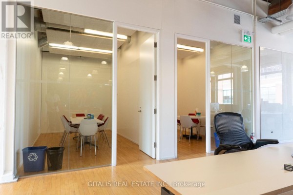Spacious open-plan office with long desks, computers, and large windows with exposed ceiling pipes. - 202a - 219 Dufferin Street, Toronto