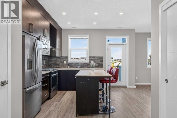 Kitchen island with red stools, stainless steel refrigerator, dark cabinets, and subway tile backsplash. - 203, 315 Redstone  Ne, Calgary