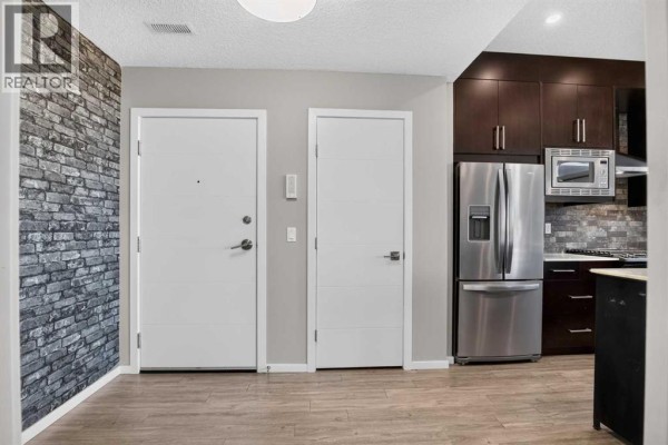 Interior hallway with two white doors, faux brick accent wall, and adjacent kitchen. - 203, 315 Redstone  Ne, Calgary