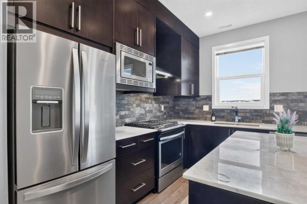 Kitchen with dark wood cabinets, stainless steel appliances, gas range, and marble-style countertop. - 203, 315 Redstone  Ne, Calgary