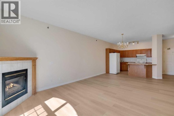 Living room with fireplace and view of open concept kitchen. - 203, 4835 Dalhousie Drive Nw, Calgary