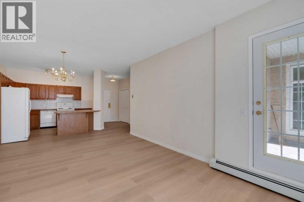 Living room with fireplace and view of kitchen and hallway. - 203, 4835 Dalhousie Drive Nw, Calgary