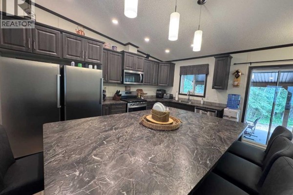 A view of the kitchen island and dark gray cabinets, with patio doors showing a wooded area. - 203, 70443 245 Range, Valleyview