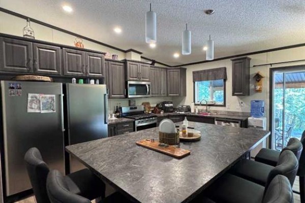 The open-concept kitchen with a large island, stainless steel appliances, and abundant dark gray cabinetry. - 203, 70443 245 Range, Valleyview