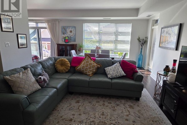 Living room with a dark green sectional sofa, colorful pillows, rug, and dining area in background. - 203 - 1 Shipyard Lane, Collingwood