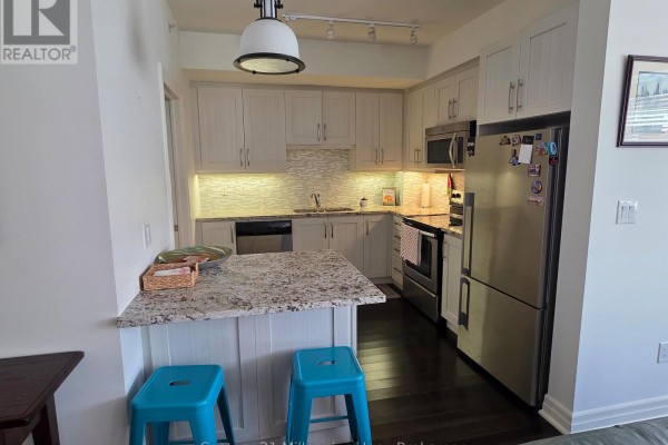 Kitchen with white cabinets, granite countertops, stainless steel appliances, and two blue bar stools. - 203 - 1 Shipyard Lane, Collingwood