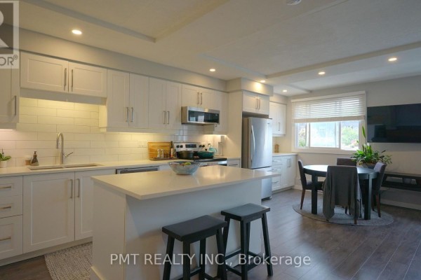 Bright white kitchen with stainless steel appliances, island, and dining area. - 203 - 10 Cooper Street, Cambridge
