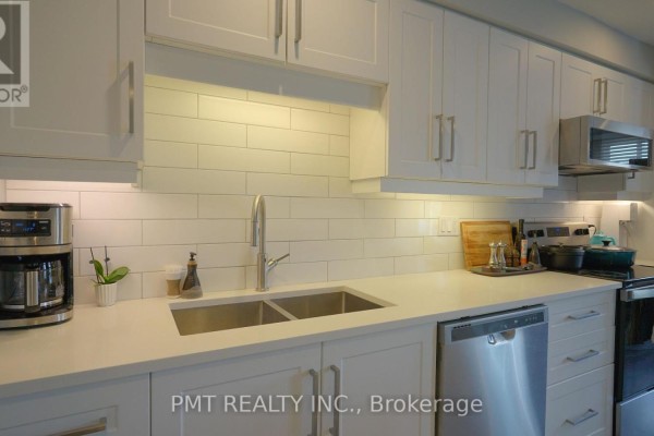 Close-up of the white kitchen countertop, double sink, and stainless steel dishwasher. - 203 - 10 Cooper Street, Cambridge