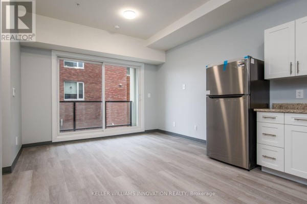 Living area with light grey walls, light wood floors, balcony view, and stainless steel refrigerator. - 203 - 10 Queen Street, St  Thomas