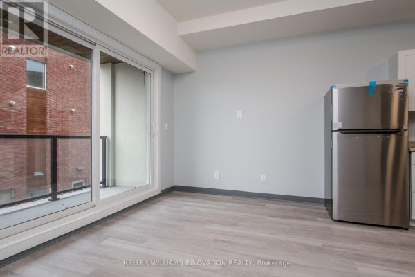 Living area with light grey walls, light wood floors, and balcony view with brick building. - 203 - 10 Queen Street, St  Thomas