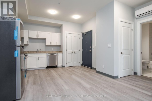 Open concept kitchen and living area with white cabinets, stainless steel appliances, and light wood floors. - 203 - 10 Queen Street, St  Thomas