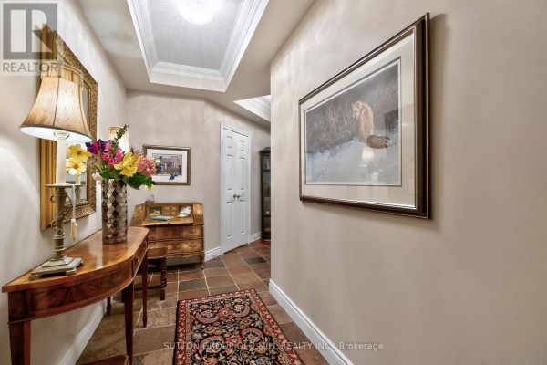 Hallway with artwork, console table, wooden chair, and patterned floor runner. - 203 - 12 Old Mill Trail, Toronto