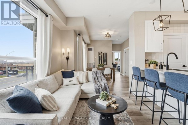 Living room and kitchen area with sectional sofa, island with bar stools, and dining area. - 203 - 120 Springvalley Crescent, Hamilton