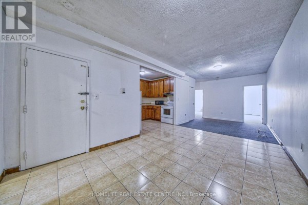 An open-concept living space with tiled floors, white walls, and an adjacent kitchen area. - 203 - 223 Jameson Avenue, Toronto