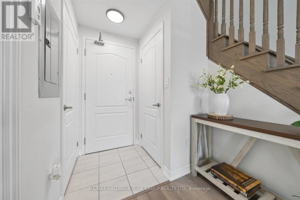 Interior hallway with white doors, tiled floor, and a wooden staircase with a console table. - 203 - 3905 Major Mackenzie Drive, Vaughan