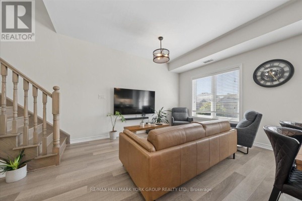Living room with a brown leather sofa, two grey armchairs, a television, and a wooden staircase. - 203 - 3905 Major Mackenzie Drive, Vaughan