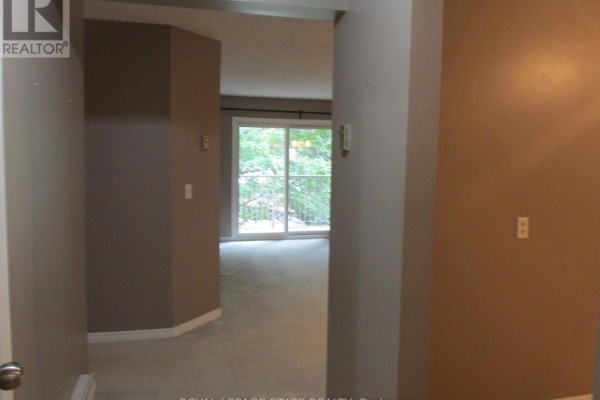 Hallway view looking into a living room with beige carpet and a sliding glass door. - 203 - 5 Niagara Street, Grimsby