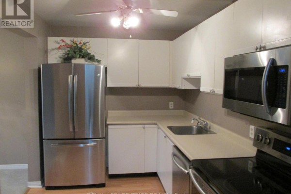Kitchen with stainless steel refrigerator, white cabinetry, and a beige countertop. - 203 - 5 Niagara Street, Grimsby