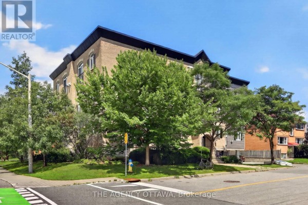 Side view of the apartment building surrounded by trees and greenery, with a street in the foreground. - 203 - 711 Churchill Avenue N, Ottawa