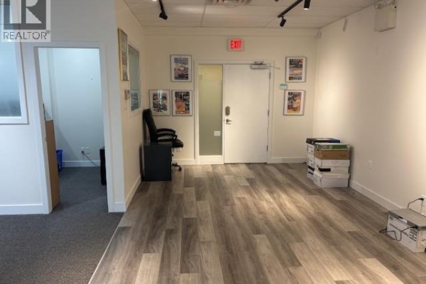 Hallway with light wood laminate flooring, white walls, framed pictures, and a door. - 203-204 8580 Cambie Road, Richmond