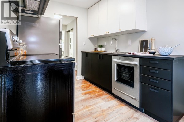 Kitchen area with a double sink, black countertops, and a small dining area with chairs. - 203 2240 Wall Street, Vancouver