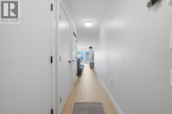 Interior hallway with light wood floors, white doors, and a glimpse of a living area. - 203 2508 Fraser Street, Vancouver