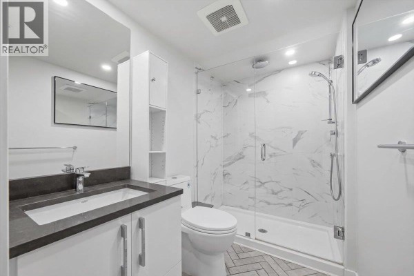 Modern bathroom with white vanity, dark countertop, and glass-enclosed shower. - 203 2508 Fraser Street, Vancouver
