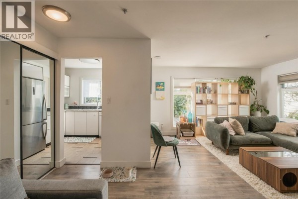 Living room with a sectional sofa, coffee table, and view into the kitchen. - 203 3230 Glasgow Ave, Saanich