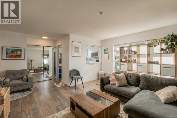 Interior view of a living room, showing furniture and a mirrored closet door. - 203 3230 Glasgow Ave, Saanich