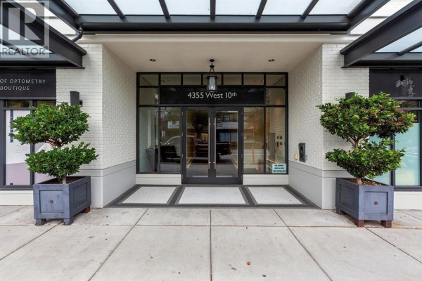 Main entrance of the apartment building with glass doors and potted trees. - 203 4355 W 10th Avenue, Vancouver