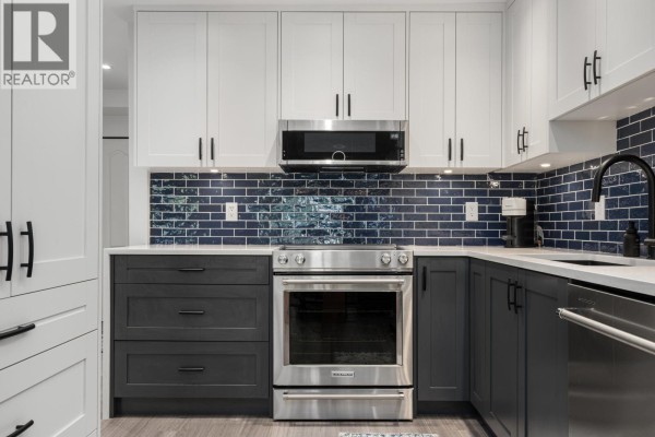 Close-up of stainless steel oven, dark grey cabinets, and blue subway tile backsplash in kitchen. - 203 825 W 15th Avenue, Vancouver