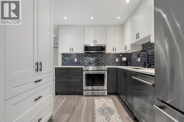 Kitchen view showing stainless steel refrigerator, dark grey cabinets, and blue tile backsplash. - 203 825 W 15th Avenue, Vancouver