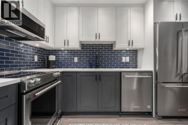 Kitchen with white cabinets, dark grey base cabinets, stainless steel oven, and blue tile backsplash. - 203 825 W 15th Avenue, Vancouver