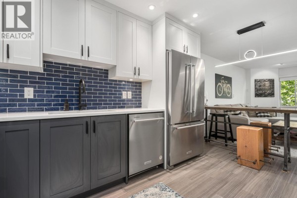 Kitchen area with stainless steel appliances, dark grey cabinets, and view of living space beyond. - 203 825 W 15th Avenue, Vancouver