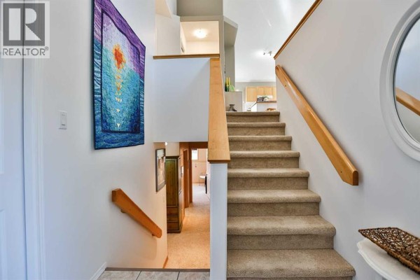 Interior staircase with beige carpet and white walls, leading to the upper floor. - 203 Blackfoot Circle W, Lethbridge
