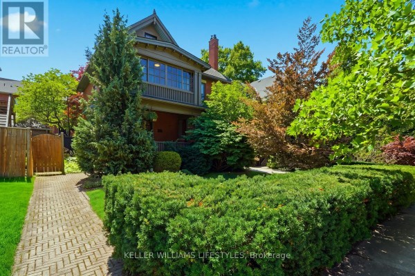 View of the brick house from the side, with a paved walkway and manicured hedges. - 203 Cheapside Street, London East