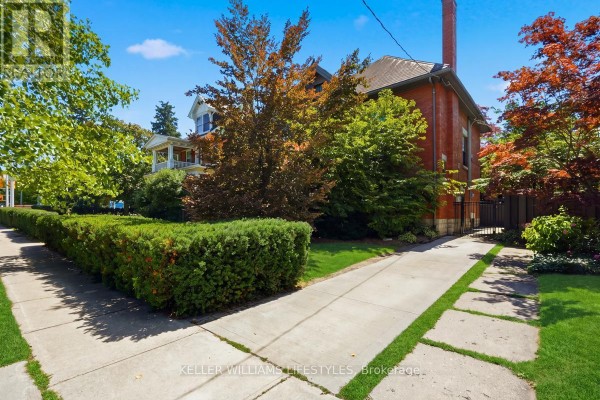 Side view of the house with a driveway and sidewalk, surrounded by trees and hedges. - 203 Cheapside Street, London East