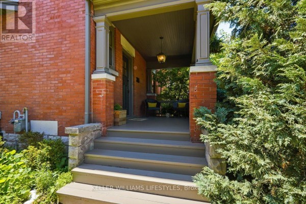 Front porch with grey steps, brick pillars, and a hanging light fixture, surrounded by greenery. - 203 Cheapside Street, London East
