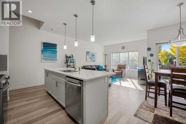 Kitchen island with stainless steel sink and dishwasher, open to living and dining area with large window. - 203 Mahogany Grove Se, Calgary