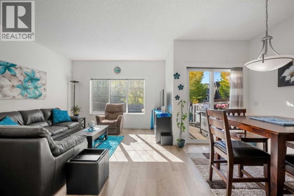 Living room with black leather sofa, recliner, coffee table, and dining area with view to deck. - 203 Mahogany Grove Se, Calgary