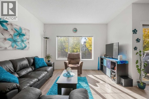 Living room featuring a black leather sofa, recliner, coffee table on blue rug, and window view. - 203 Mahogany Grove Se, Calgary