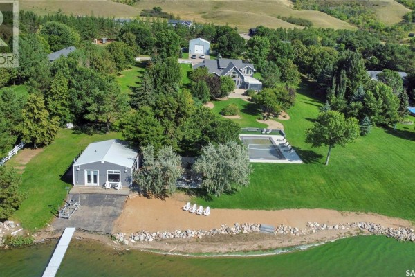 Aerial view of a house, pool, garage, dock, and beach area by a lake, surrounded by trees and green hills. - 203 North Shore Drive, North Grove