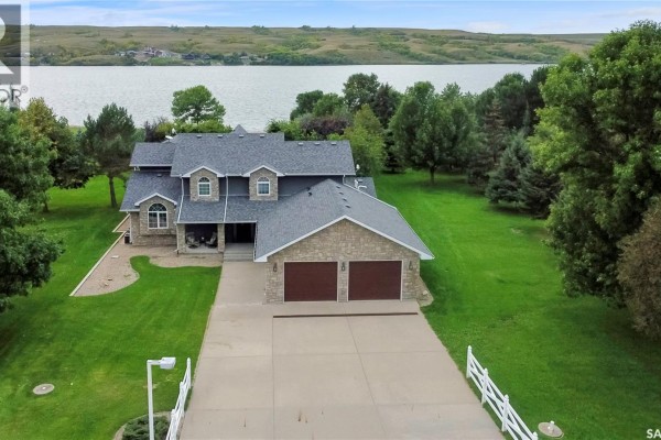Drone shot of a two-story house with dual garage doors and stone facade, set on a wide lawn with lake backdrop. - 203 North Shore Drive, North Grove