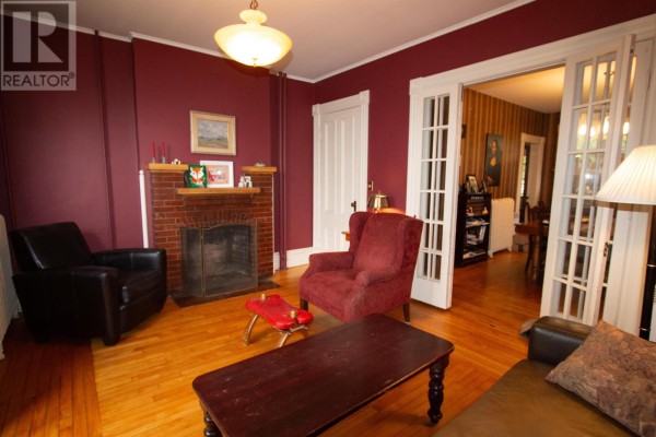 Living room with a brick fireplace, burgundy walls, and access to another room. - 203 Notre Dame Street, Summerside