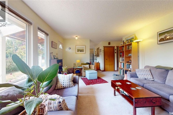 Living room with beige carpet, blue sofas, wooden coffee table, and large windows. - 203 Pottery Street, Eastend